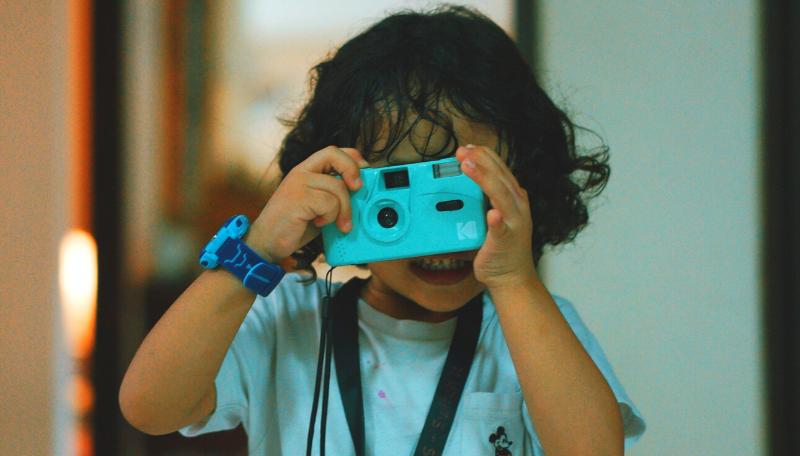Ein Kind schaut durch eine kleine blaue Kamera.