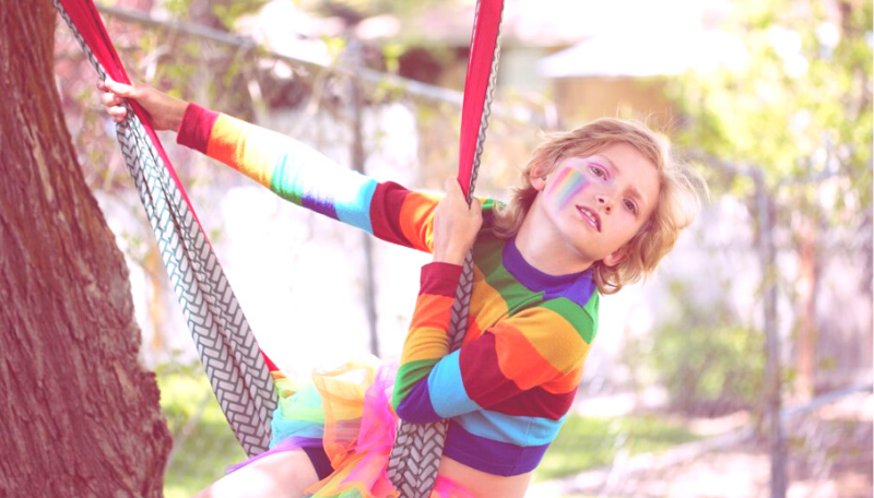 Ein Kind im Regenbogenpulli schaukelt auf einer Hängematte.