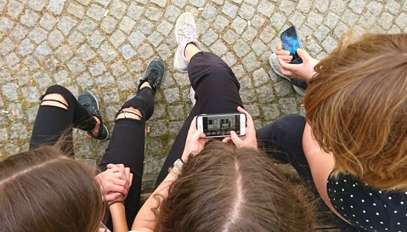 Drei Jugendliche schauen sich gemeinsam ein Bild auf einem Smartphone an.