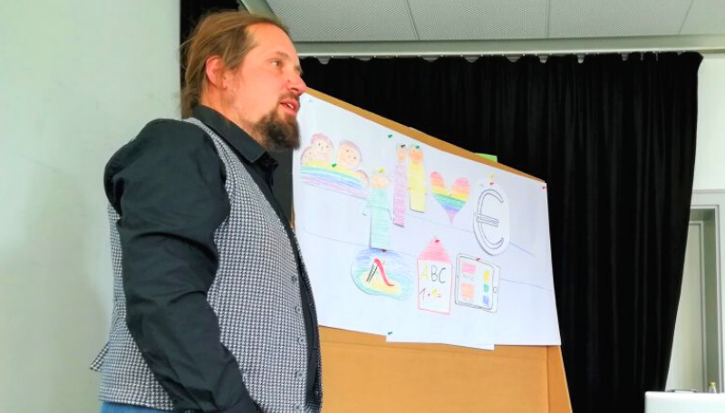 Markus Nau steht neben einer Collage und referiert.