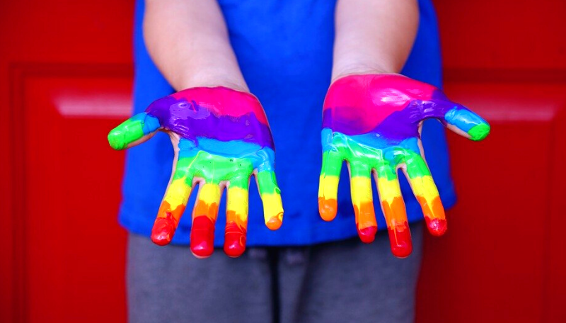 Ein Kind hält seine bunt in Regenbogenfarben bemalten Hände in die Kamera.