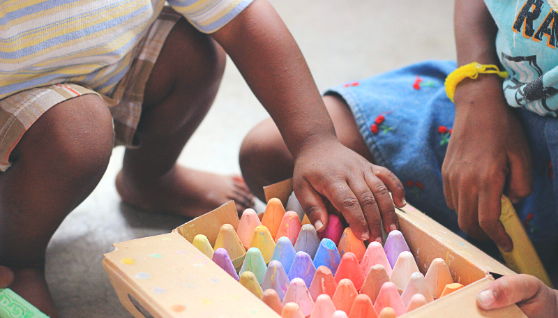 Zwei Kinder greifen in einer Kiste voll bunter Straßenkreide.