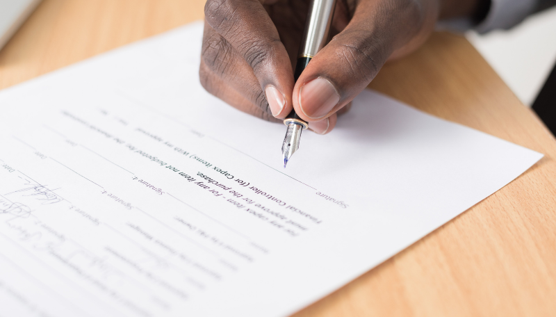 Eine Hand unterschreibt mit einem Füller ein Dokument.
