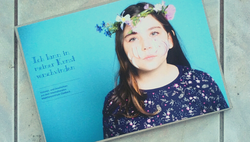 Blaues Buch auf dem ein Mädchen* mit Blumenkranz abgebildet ist.