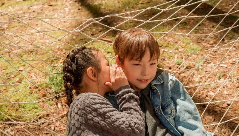 Ein Kind flüstert einem anderen Kind etwas ins Ohr.