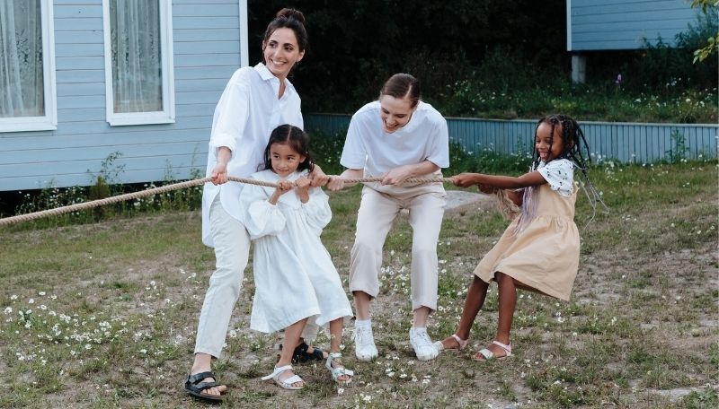 Zwei erwachsene Personen und zwei Kinder ziehen lachend gemeinsam an einem Tau.